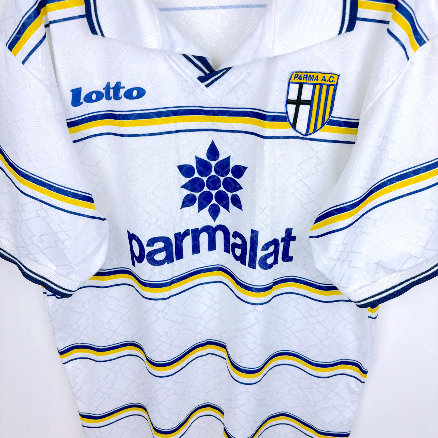 Angled close up of retro football shirt by Parma AC produced by Lotto. White body featuring blue and yellow hoops.