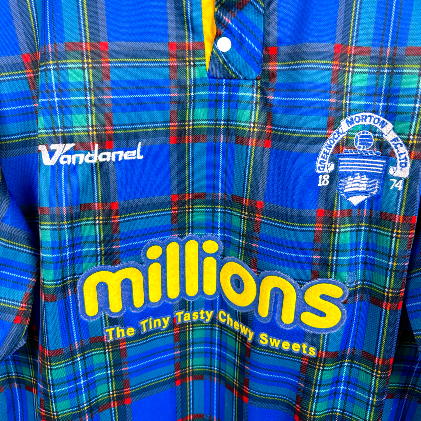 Close up view of Greenock Morton retro soccer jersey produced by Vandanel. Tartan design with yellow 'Millions' candy logo and embroidered Greenock crest.