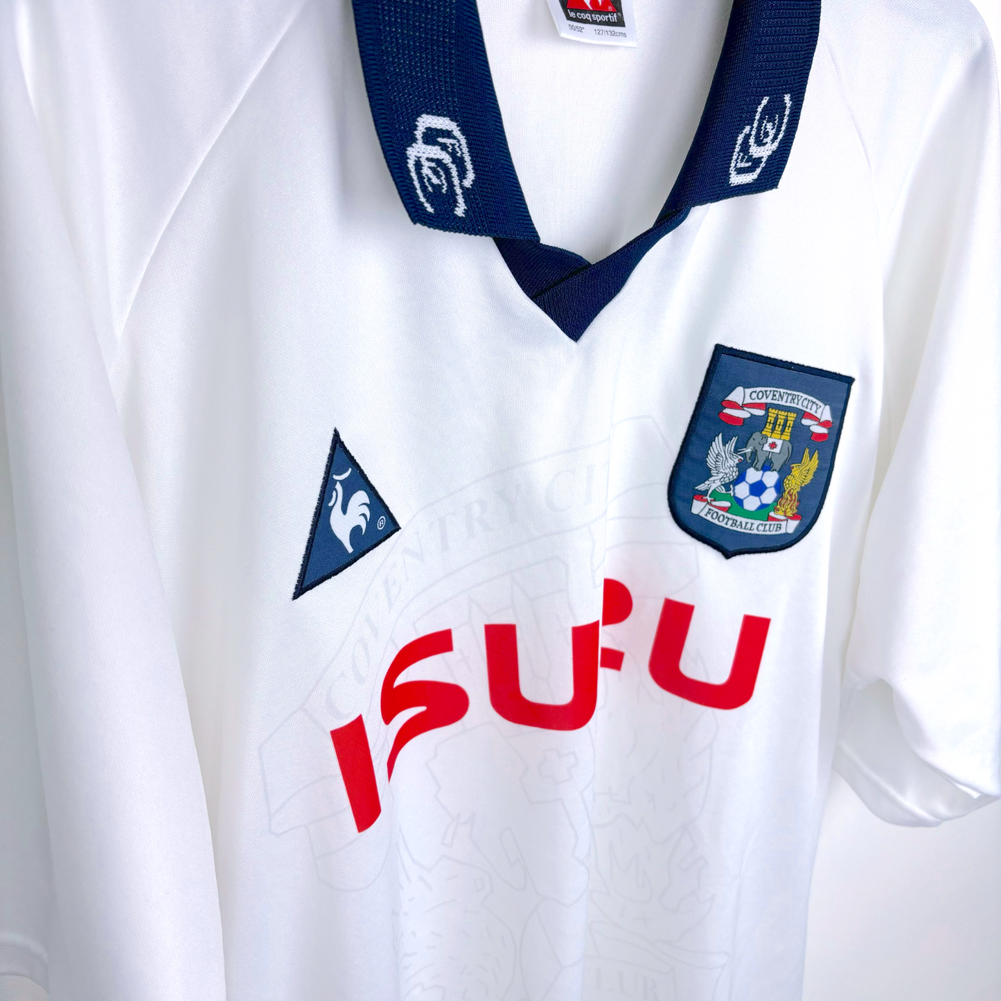 Side view of white Coventry City vintage football shirt with navy collar. Produced by le coq sportif, it features an embroidered Coventry badge with red Izuzu sponsor.