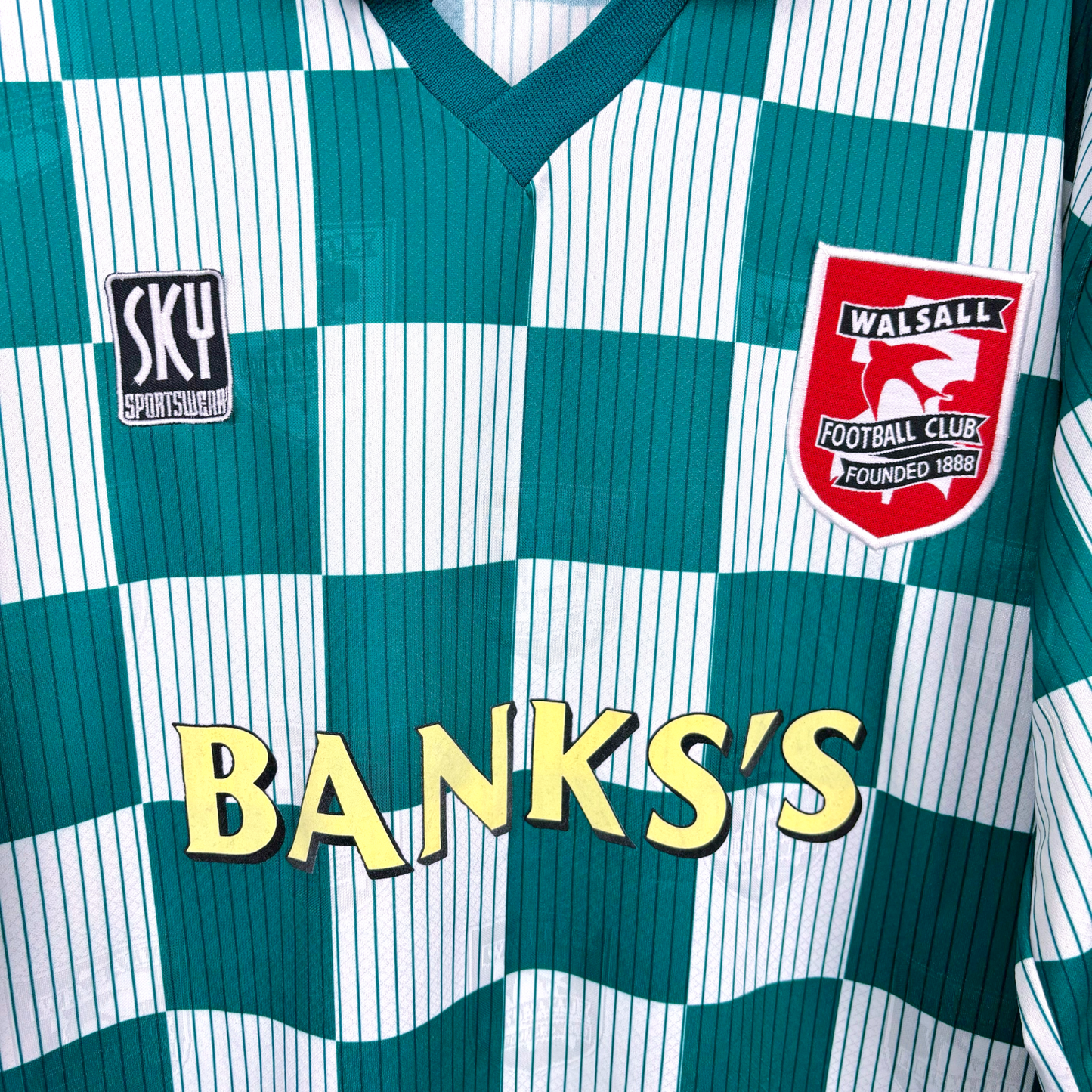 Close up of Walsall retro soccer jersey produced by Sky Leisure. Check green and off-white pattern with Banks's yellow sponsor. Embroidered club crest.