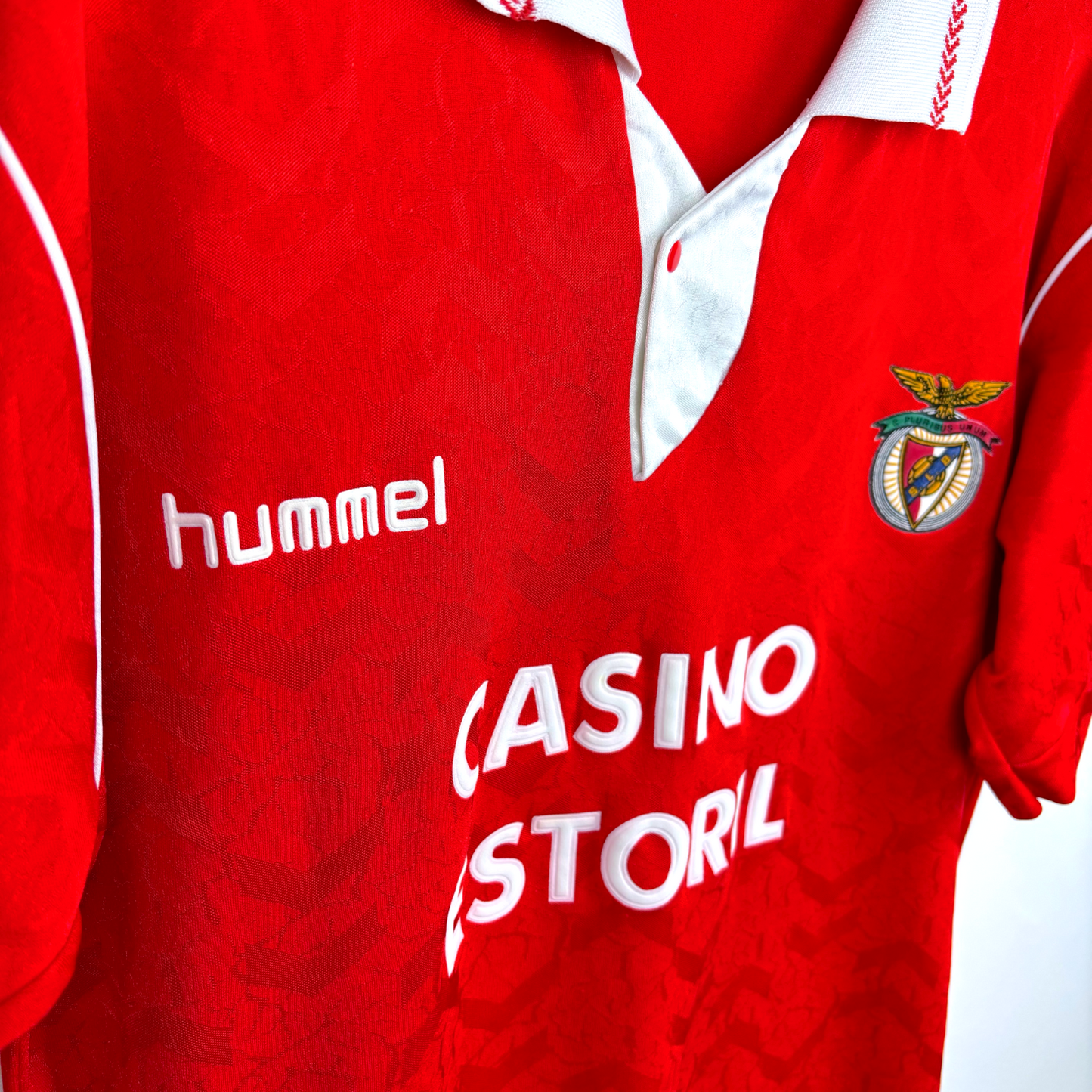 Side view of vintage Benfica home football shirt 'hummel' and 'Casino Estoril' text, featuring Benfica club crest. Red body with white trim.