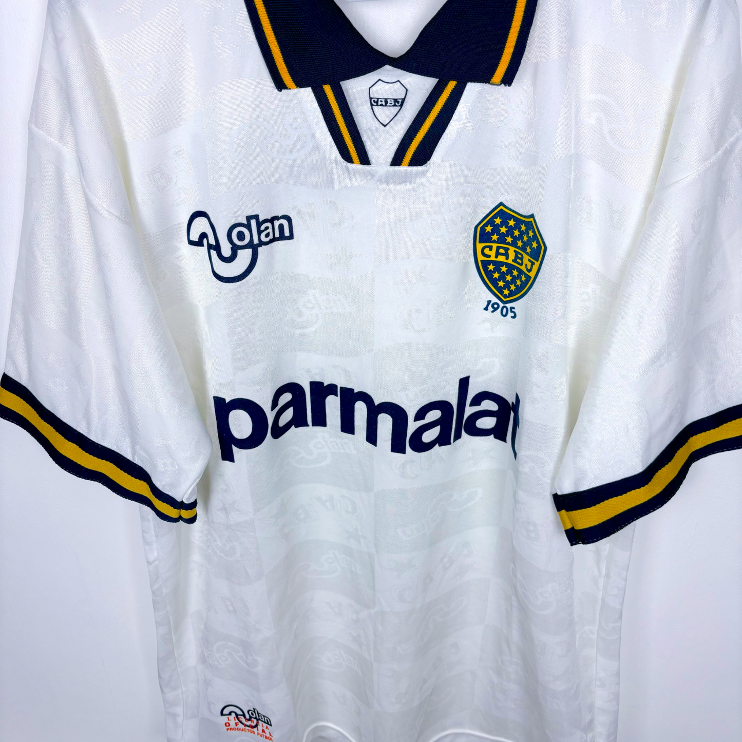 Downward view of Boca Juniors 1995-1996 away vintage soccer jersey produced by OLAN. White body featuring navy and gold accents.