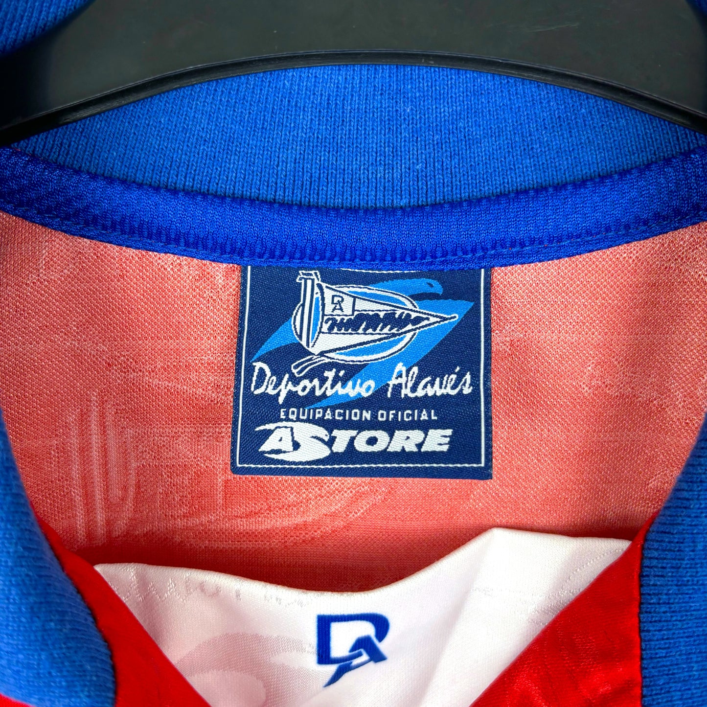 Close-up of the collar on the Deportivo Alavés 1994-1999 Away Football Shirt by Astore, featuring the club's logo, Spanish text, and a blue collar with red and white lining from this Basque team's classic shirt.