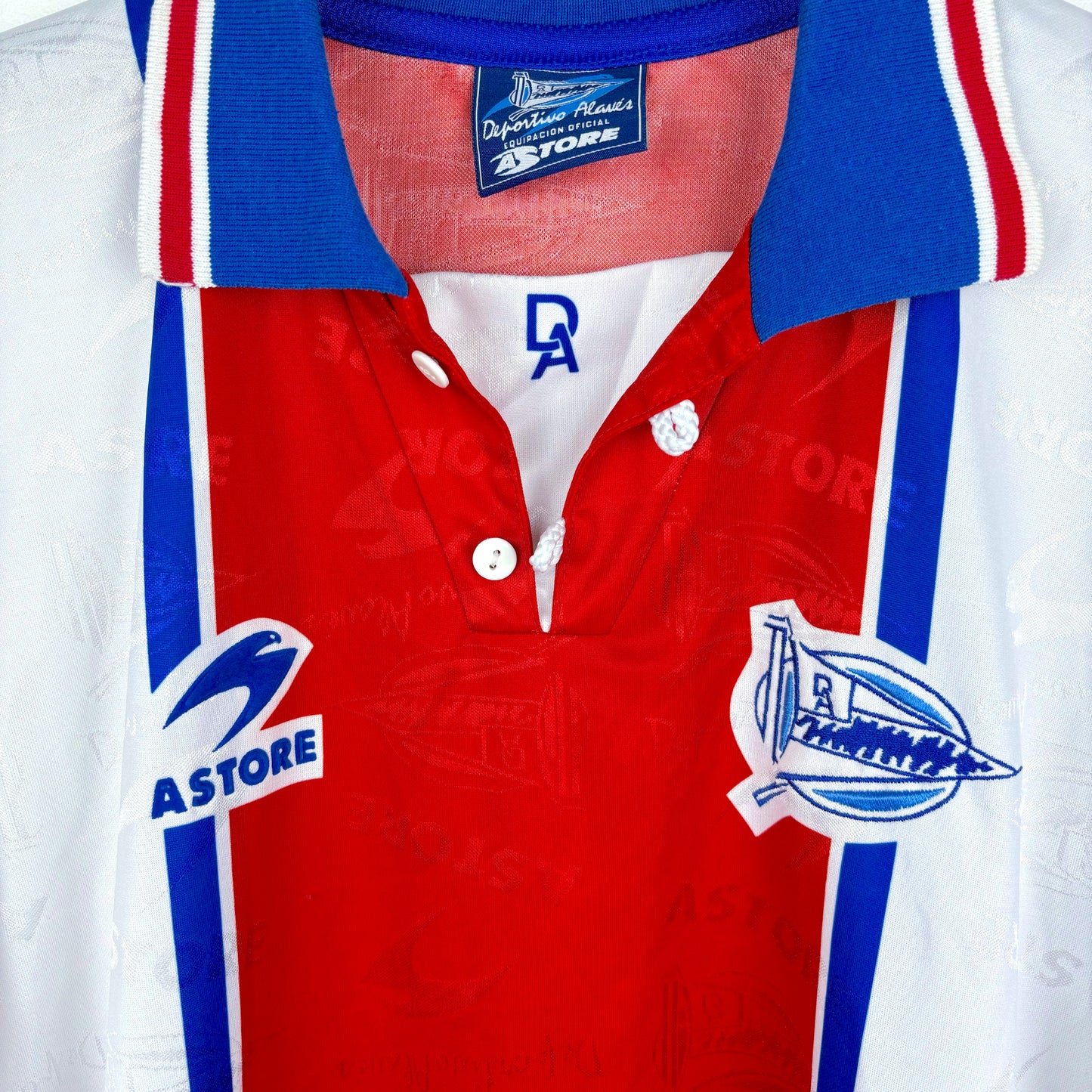 Close-up of the Deportivo Alavés 1994-1999 Away Football Shirt by Astore, featuring a collared design with red, white, and blue stripes, ASTORE logo, stylized boat crest, and "Deportivo Alavés" tag.