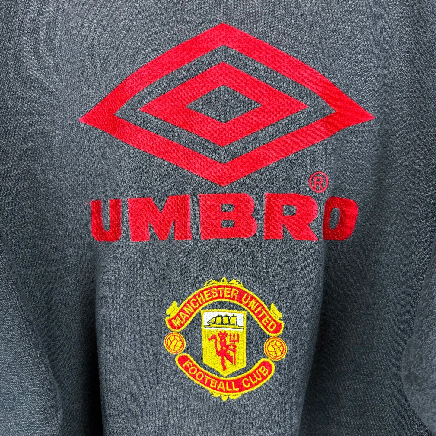 Close-up of Umbro logo and Manchester United crest on grey sweatshirt – vintage retro football sweatshirt.
