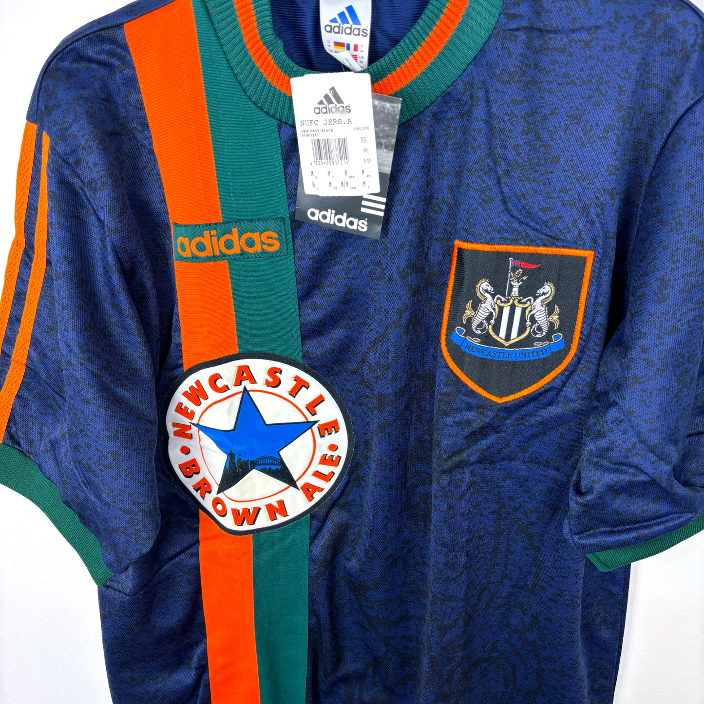 Side view of Newcastle United retro football shirt produced by Adidas. Navy body featuring duel green and orange stripes and crew neck collar.