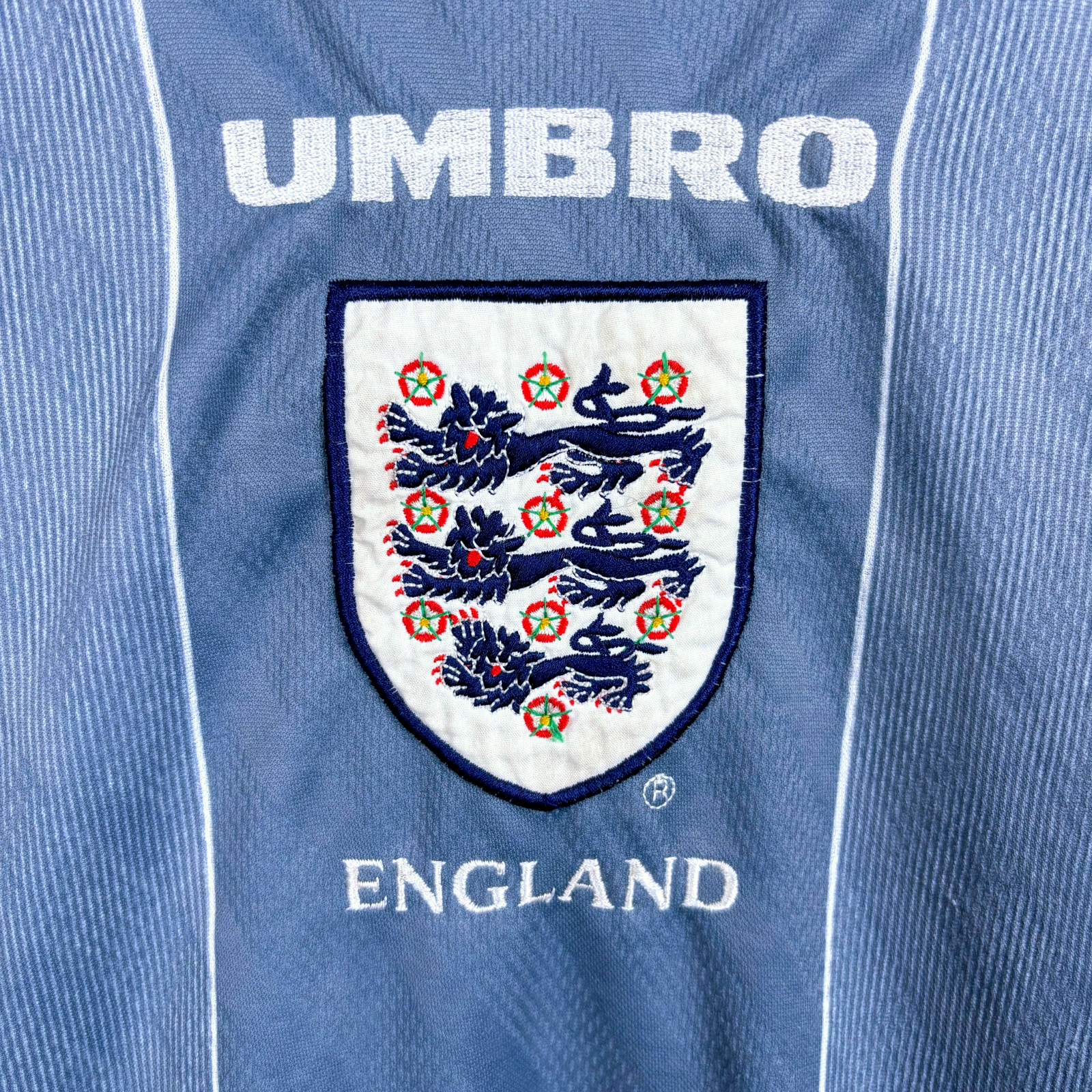 Close up view of fully embroidered Three Lions crest and Umbro writing on an England retro football shirt produced by Umbro. 