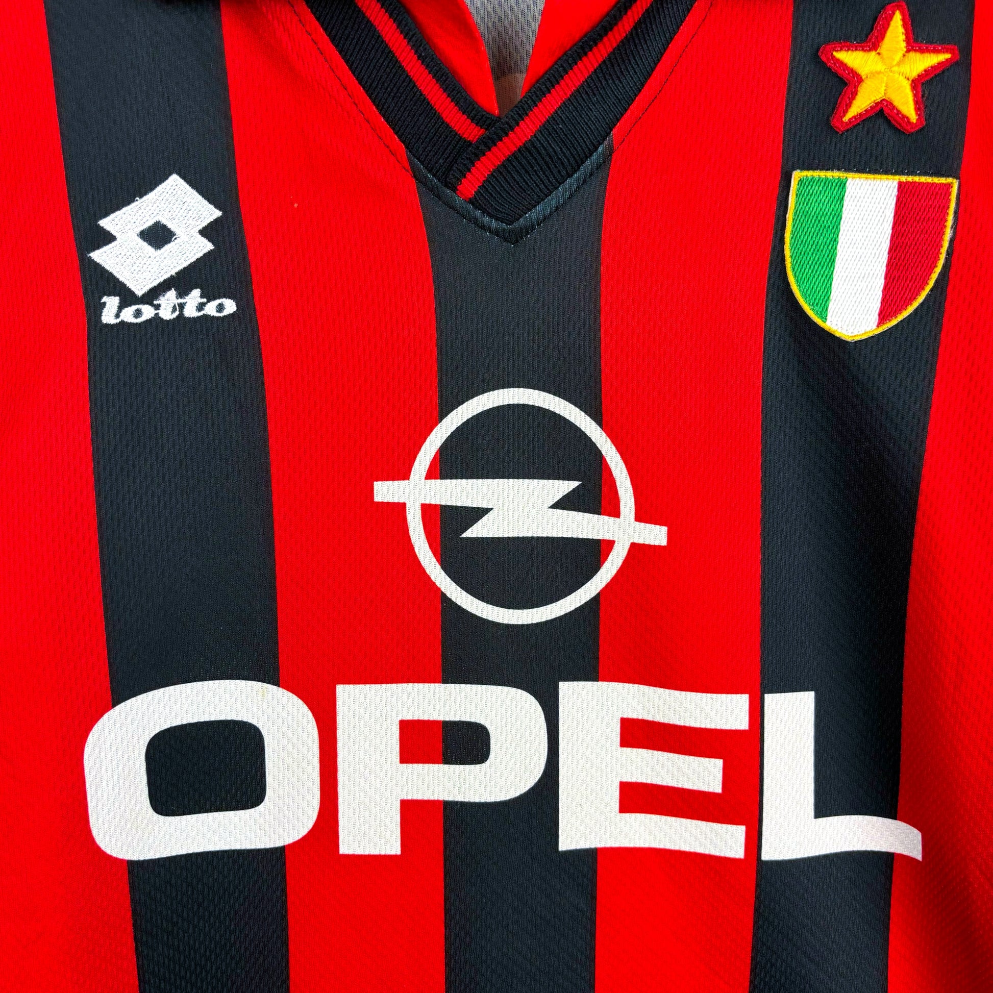 Close-up of badges on AC Milan 1996-1997 Lotto home retro soccer jersey. Red and black stripes with sublimated OPEL sponsor.