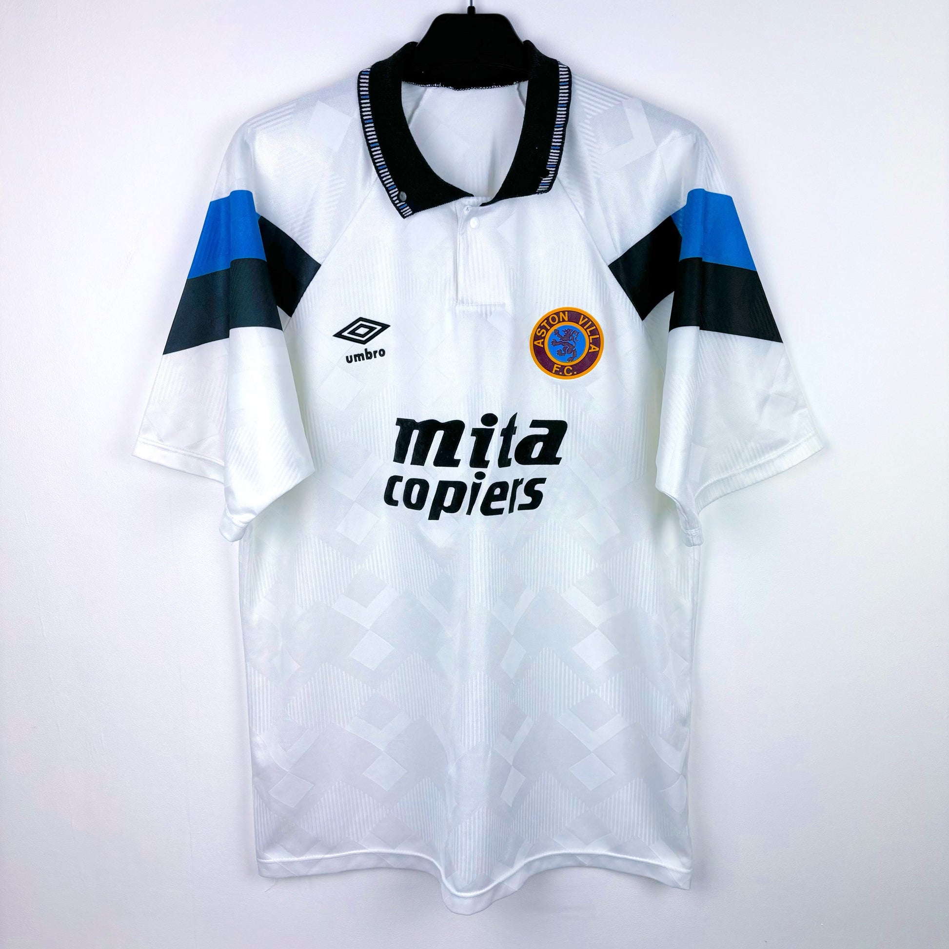 Aston Villa 1990-1993 away retro soccer jersey made by Umbro. Sublimated jacquard pattern ion white body. Black and blue trim with black Mita Copiers sponsor.
