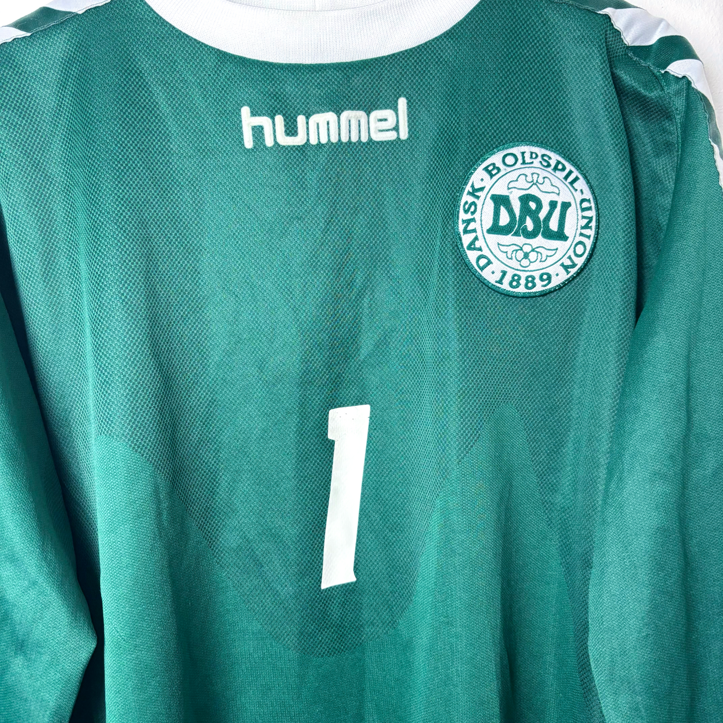 Close up view of Denmark 2002 goalkeeper/third retro soccer jersey made by Hummel. Forest green body coupled with tapered sleeves donning the classic Hummel chevrons. Embroidered Denmark badge.