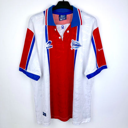 The Astore Deportivo Alavés 1994-1999 away football shirt is a vintage white, red, and blue short-sleeve jersey with a collared neck, club and sponsor logos, and La Liga badge, displayed on a black hanger.