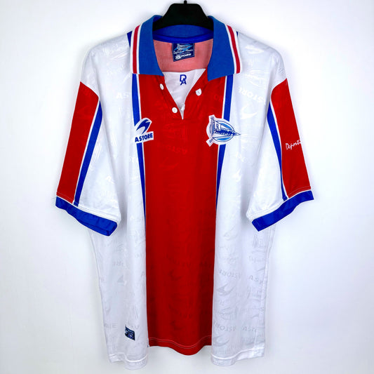 The Astore Deportivo Alavés 1994-1999 away football shirt is a vintage white, red, and blue short-sleeve jersey with a collared neck, club and sponsor logos, and La Liga badge, displayed on a black hanger.