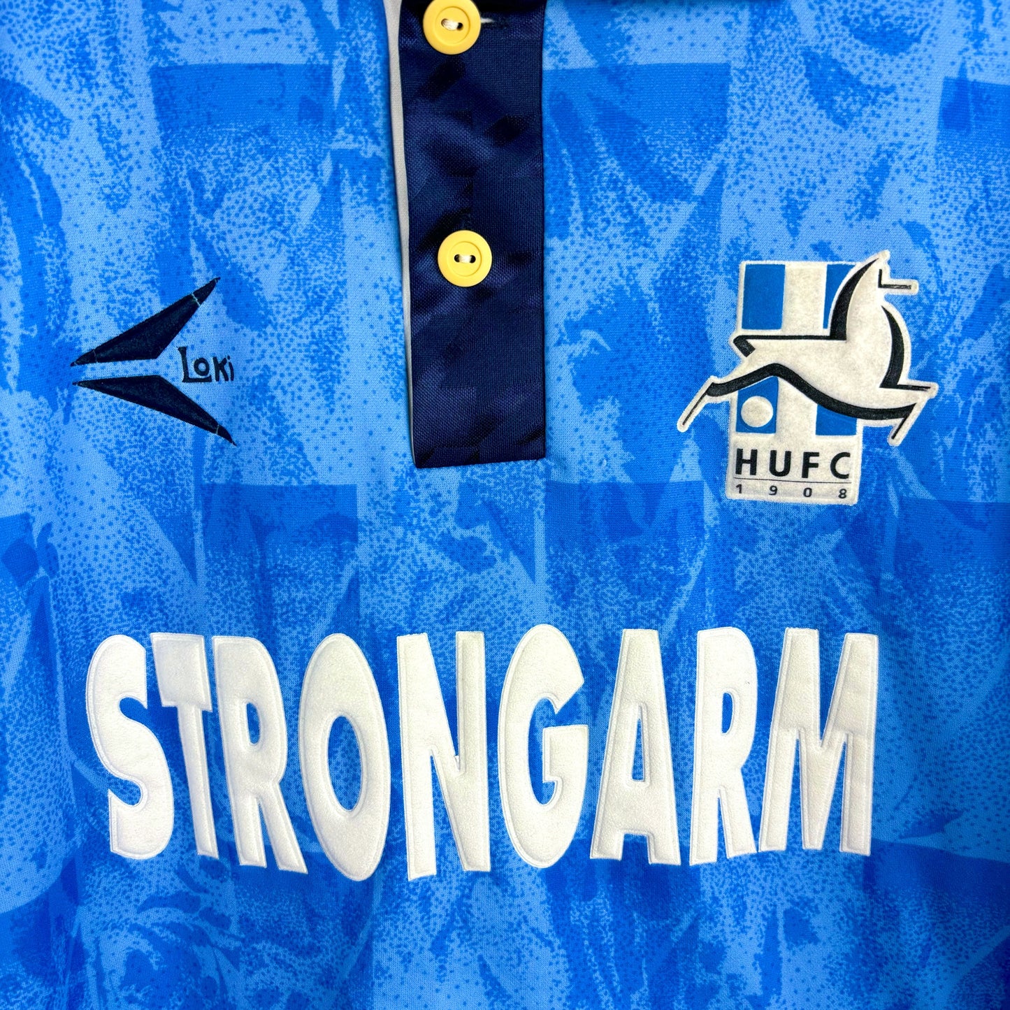 Close up view of Hartlepool United 1993-1995 retro football shirt with 'Strongarm' sponsor and hart club badge. Blue body with navy trim and collar. 
