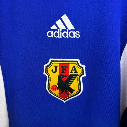 Close up of embroidered badge on Japan 1999-2000 adidas vintage soccer sweatshirt. Blue body with white vertical swooshes and red trim. Brand new with tags attached. 