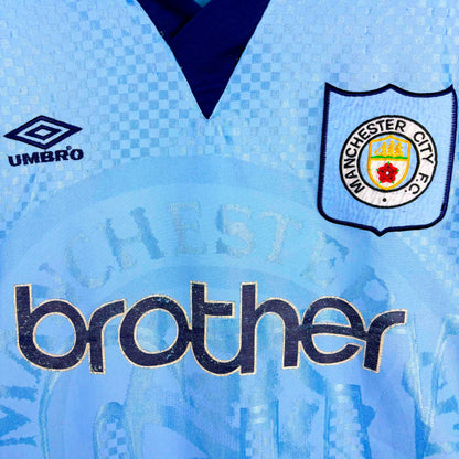 Close up of badges and Brother sponsor on Man City 1995-1997 Umbro home vintage football jersey. Sky blue body with sublimated checkered pattern.