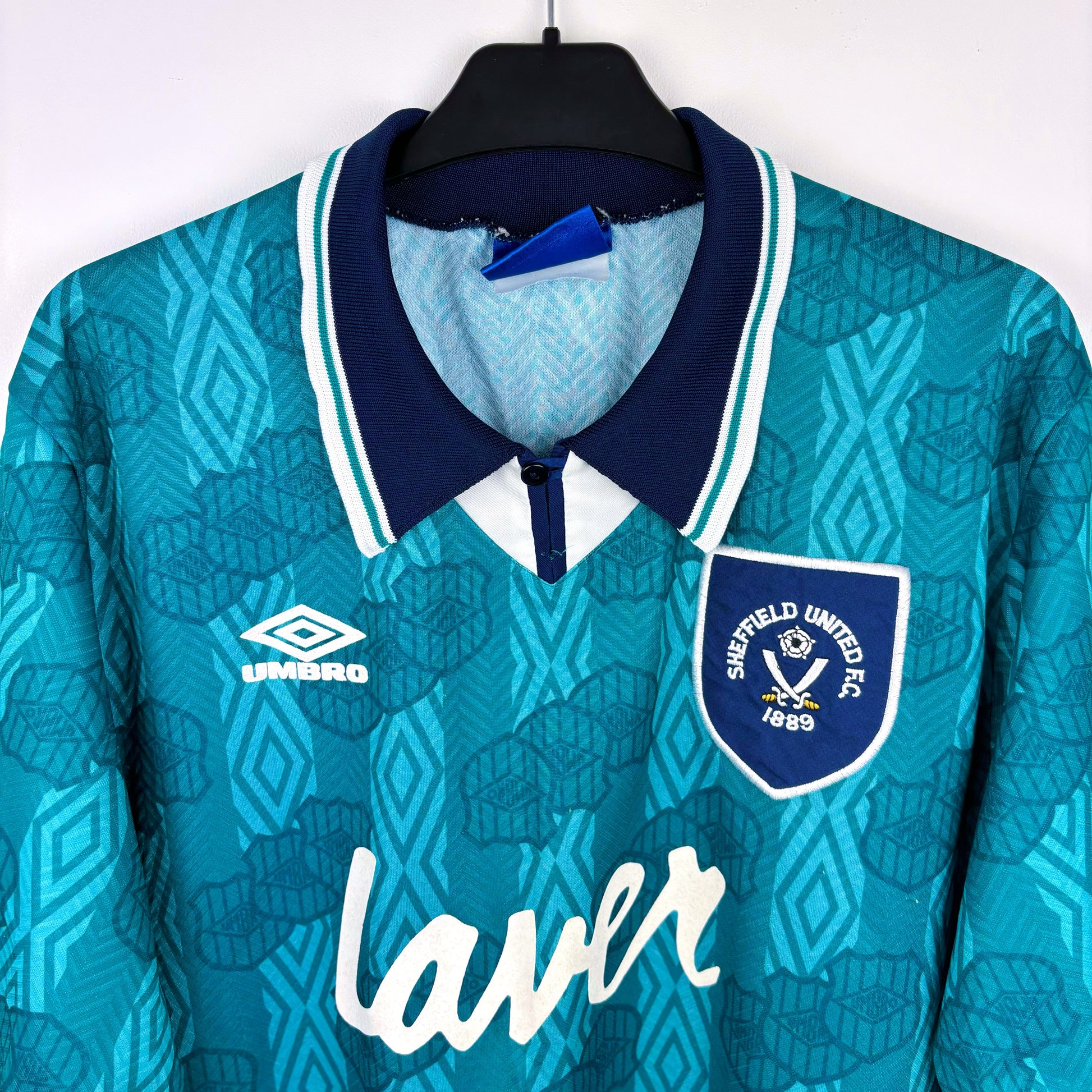 Teal sports jersey with navy collar and 'Sheffield United FC' badge on a hanger.